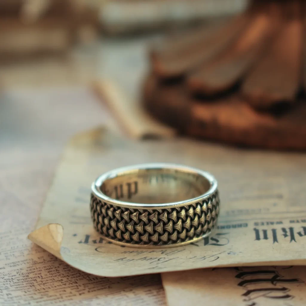 The image features a beautifully handcrafted promise ring from Silveringdom, resting elegantly on an aged piece of paper. This ring showcases an intricate androgynous design, making it suitable for anyone, regardless of gender. The fine details and smooth finish highlight the exceptional craftsmanship involved in creating this piece. Silveringdom offers the unique opportunity to customize these promise rings, allowing you to create a piece that truly represents your personal style and the meaningful commitments you cherish. This image captures the essence of Silveringdom’s dedication to creating elegant, meaningful jewelry that celebrates love and unity.