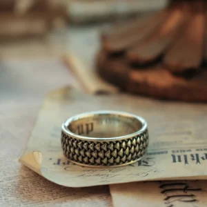 The image features a beautifully handcrafted promise ring from Silveringdom, resting elegantly on an aged piece of paper. This ring showcases an intricate androgynous design, making it suitable for anyone, regardless of gender. The fine details and smooth finish highlight the exceptional craftsmanship involved in creating this piece. Silveringdom offers the unique opportunity to customize these promise rings, allowing you to create a piece that truly represents your personal style and the meaningful commitments you cherish. This image captures the essence of Silveringdom’s dedication to creating elegant, meaningful jewelry that celebrates love and unity.