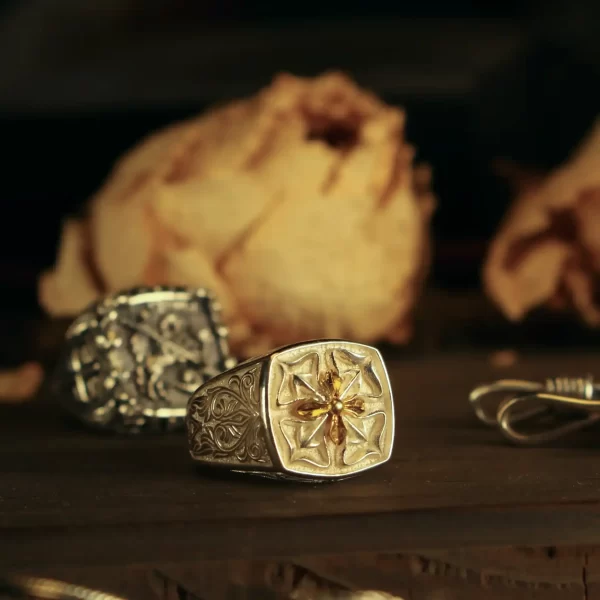 The image features a pair of matching rings from Silveringdom, each crafted in a light silver hue. The rings are elegantly designed, with one prominently displaying a four-leaf clover at its center, symbolizing luck and prosperity. The clover is intricately detailed, adding a touch of charm and sophistication. The second ring, slightly blurred in the background, mirrors the design, emphasizing the unity and harmony of the set. Both rings are set against a dark, warm backdrop that enhances their light silver shine, making them stand out beautifully. These matching rings from Silveringdom are perfect for couples seeking a blend of elegance and meaningful symbolism in their jewelry.