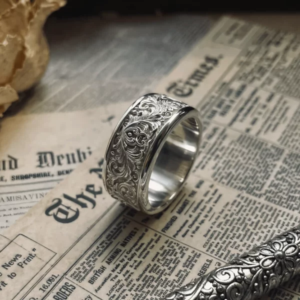 This exquisite piece from Silveringdom showcases a light silver ring adorned with intricate scrollwork in relief. The delicate patterns create a sense of timeless elegance, making it a perfect addition to any jewelry collection. The craftsmanship is evident in the detailed design, which highlights the beauty of the matching rings concept. The ring’s scrollwork adds a touch of sophistication, while the relief work gives it a three-dimensional effect, enhancing its visual appeal. This piece embodies the essence of Silveringdom, where every item is crafted with precision and care, ensuring that each ring is not just a piece of jewelry, but a work of art. Ideal for those who appreciate fine craftsmanship and elegant design.
