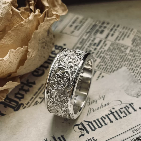 This stunning Silveringdom creation features a pair of matching rings in light silver, adorned with intricate scrollwork in relief. The delicate patterns, reminiscent of vintage artistry, add a touch of timeless elegance and sophistication. The scrollwork design creates a three-dimensional effect, enhancing the visual appeal and highlighting the fine craftsmanship. The light silver material catches the light beautifully, adding a subtle shimmer that draws attention to the intricate details. These rings are a perfect symbol of unity and elegance, embodying the essence of Silveringdom where each piece is meticulously crafted to perfection. Ideal for those who appreciate exquisite design and fine craftsmanship, these rings are a testament to the artistry and dedication of the craftsmen.
