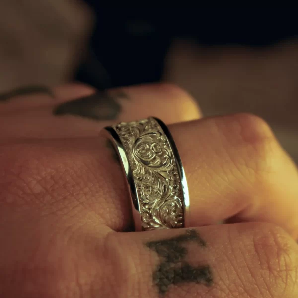 These matching rings from Silveringdom are a stunning example of fine craftsmanship. Each ring features intricate scrollwork in relief, creating a three-dimensional effect that highlights the delicate patterns. The light silver finish adds a touch of elegance, making these rings perfect for any occasion. The rings are shown on a finger, emphasizing their beauty and fit. The soft lighting enhances the light silver hue, casting gentle shadows that bring out the details in the scrollwork. These matching rings are not just pieces of jewelry but symbols of timeless elegance and sophistication, perfect for those who appreciate the artistry of Silveringdom.