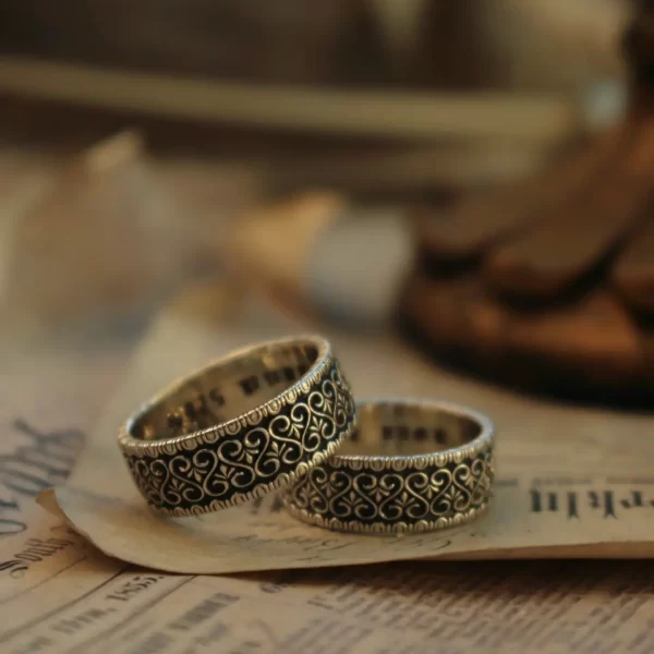 In the heart of Silveringdom’s artisan workshop, a pair of dark silver wedding rings gleams with timeless elegance. These rings, part of the Vintage Vow collection, are a testament to the art of handcraft. Each ring is meticulously crafted, showcasing intricate patterns that reflect the dedication and skill of our artisans. The dark silver hue adds a touch of sophistication, making these rings a perfect choice for those seeking a gender-neutral design. At Silveringdom, we understand that every love story is unique, which is why we offer the option to customize these wedding rings to match your personal style and story. Whether you’re celebrating a wedding, an anniversary, or a special bond, these rings symbolize a commitment that transcends time. Embrace the beauty of handcrafted jewelry with Silveringdom, where every piece is made with love and precision.
