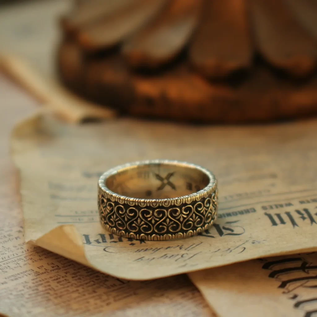 In the heart of Silveringdom, a vintage vow is beautifully captured in this image of exquisite wedding rings. The ring, crafted from dark silver, showcases the meticulous art of handcraft. Its intricate design speaks to a gender-neutral aesthetic, making it a perfect symbol for any couple. The band is adorned with delicate patterns, reflecting the timeless elegance and attention to detail that Silveringdom is renowned for. Each ring is a bespoke creation, allowing couples to customize their symbols of love to reflect their unique bond. This piece harmonizes tradition with modernity, embodying a perfect blend of strength and delicacy. Resting on an aged page, the ring tells a story of love that transcends time, making it a cherished heirloom for generations to come.