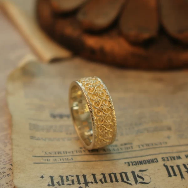 In the heart of Silveringdom, a stunning vintage vow is captured in this image of a handcrafted engagement ring. The ring, made from light silver, showcases intricate designs that reflect the artistry of a bygone era. This androgynous piece is perfect for those who appreciate timeless elegance and the beauty of detailed craftsmanship. Each ring is meticulously handcrafted, ensuring that no two pieces are exactly alike. The ability to customize these engagement rings allows for a personal touch, making each ring a unique symbol of love and commitment. The light silver band, with its delicate engravings, stands out as a testament to the skill and dedication of the artisans at Silveringdom. Whether you’re looking for a ring that tells a story or one that simply exudes classic charm, this engagement ring from Silveringdom is a perfect choice.