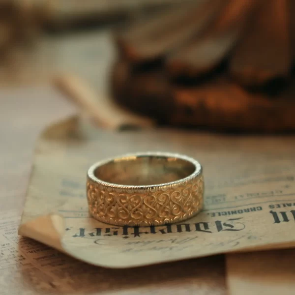 In the heart of Silveringdom’s vintage vow collection lies a stunning display of handcraft mastery, a pair of wedding rings that embody the essence of timeless commitment. These bands, with their intricate patterns and light silver hue, speak volumes of the meticulous attention to detail and skill involved in their creation. The design is gender-neutral, catering to all who wish to express their love without the confines of traditional aesthetics. Each ring is a testament to the artistry that Silveringdom prides itself on—rings that are not merely worn but cherished as heirlooms. The ability to customize these pieces ensures that each set is as unique as the bond it symbolizes. Set against an aged parchment backdrop with elegant script, these rings are not just jewelry; they are a celebration of love’s enduring promise captured in silver.
