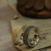 In the image, two beautifully crafted wedding rings are showcased, embodying the essence of ‘silveringdom.’ The ring on the left, with its light silver hue, features intricate patterns that evoke a sense of a vintage vow, highlighting the artistry of handcraft. Its counterpart, in dark silver, boasts a unique design that speaks to the meticulous customization involved. Both rings are gender-neutral, making them perfect for any couple seeking a timeless symbol of their union. The contrast between the light silver and dark silver rings not only accentuates their individual beauty but also complements them as a harmonious pair. These wedding rings are a testament to the blend of traditional craftsmanship and modern design, offering a personalized touch that caters to diverse tastes and preferences.