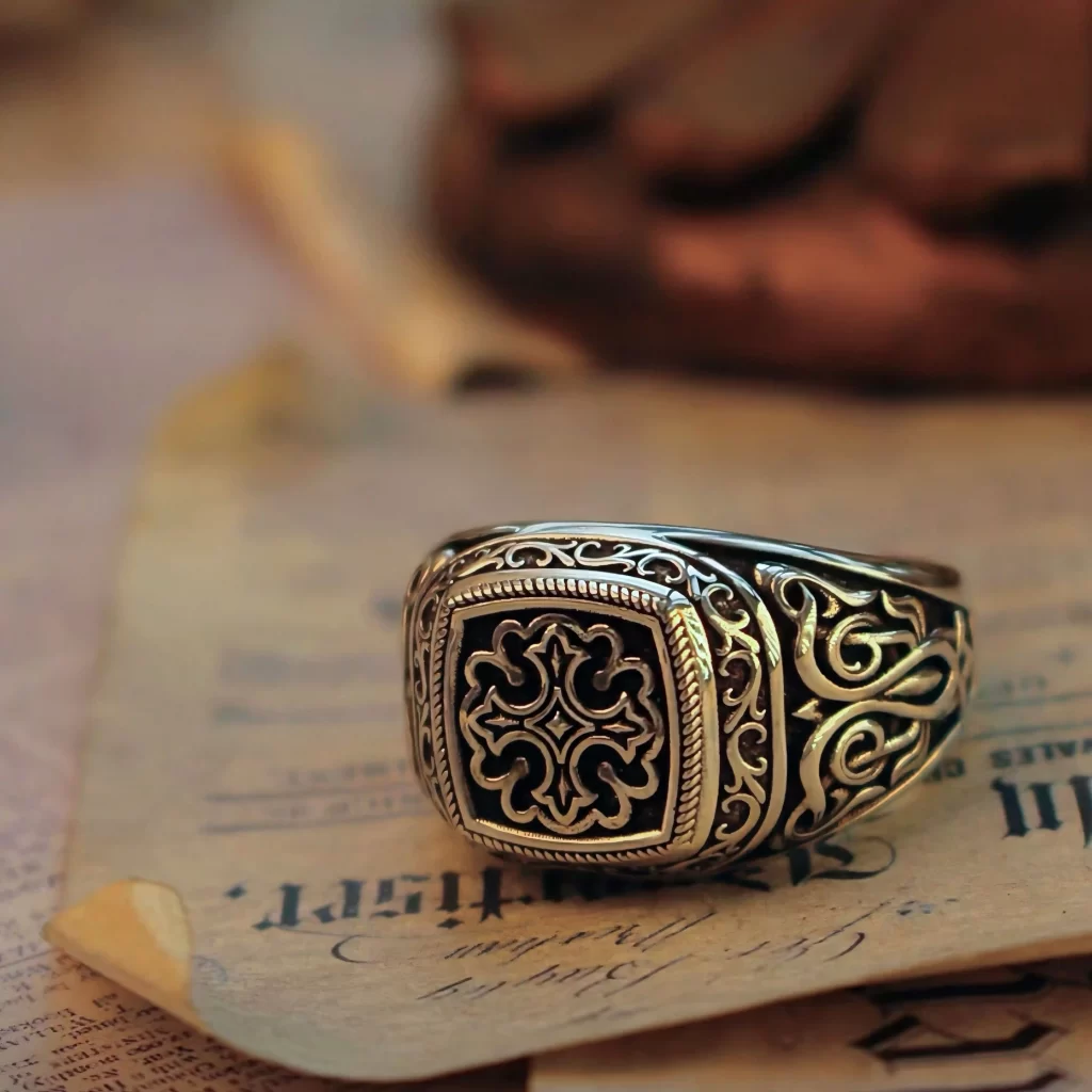 The image features a stunning silver ring from Silveringdom. This ring showcases intricate totem-inspired engravings, reflecting a blend of medieval artistry and modern elegance. The detailed craftsmanship highlights the ring’s unique design, making it a standout piece. The silver band gleams with a polished finish, adding a touch of sophistication. This ring is part of a collection of matching rings, perfect for couples or friends who appreciate historical symbolism and refined style. This piece beautifully represents Silveringdom’s commitment to quality and timeless design in their silver rings collection.